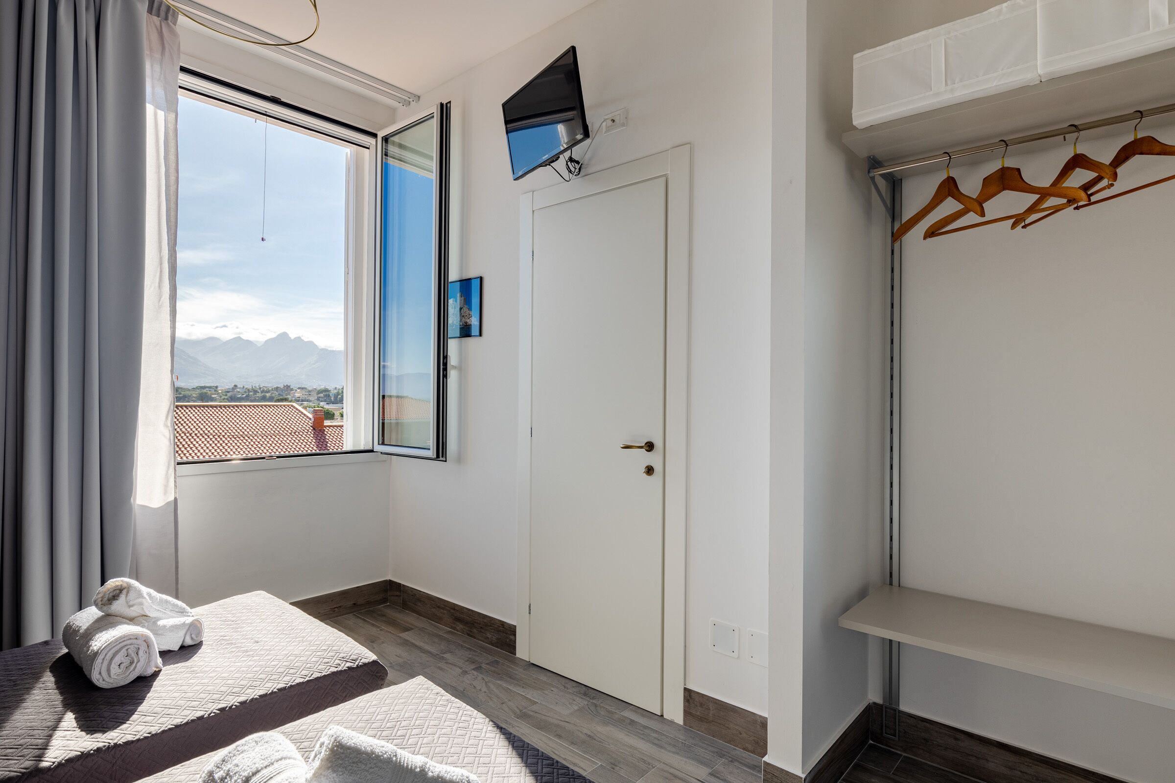 A hotel room with a bed, a TV mounted on the wall, a door, and a window with a mountain view.
