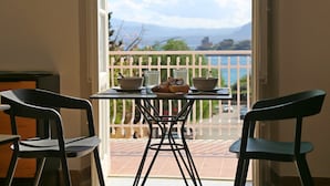 A balcony with a table set for breakfast, two chairs, and a view of a body of water and mountains. - Villa Edera Rental Rooms (Santa Flavia)