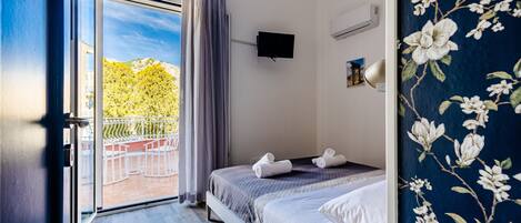 A bedroom with a bed, a TV, and a balcony with a view of trees.