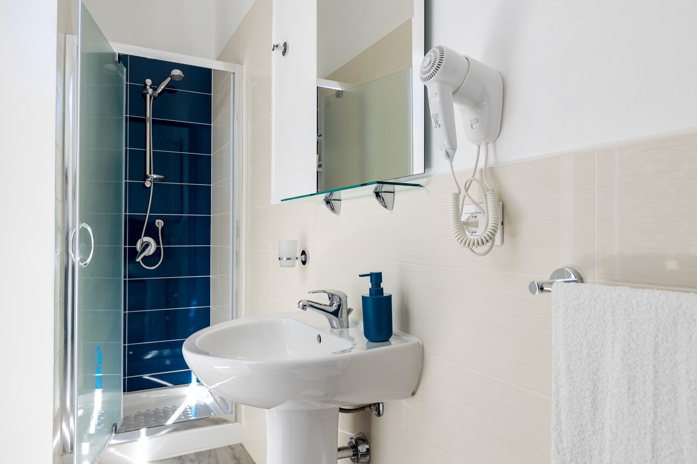 Une salle de bain avec une douche à parois de verre, un lavabo blanc, un miroir et un sèche-cheveux fixé au mur.
