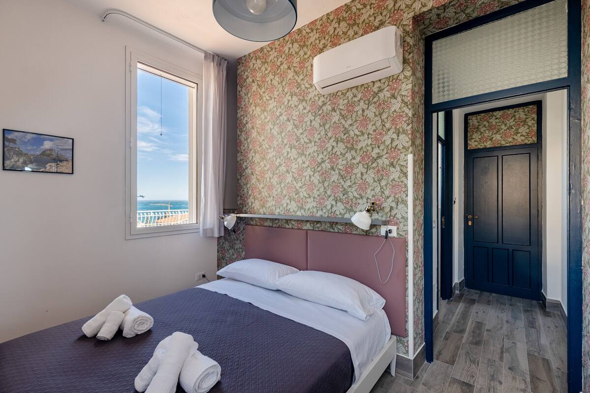 A bedroom with a bed, towels, a window, an air conditioner, and a door.