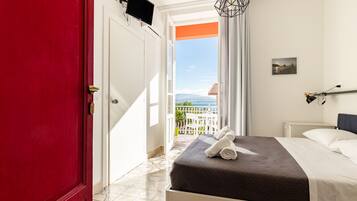 A hotel room with a bed, a TV, a view of the sea, and a balcony.