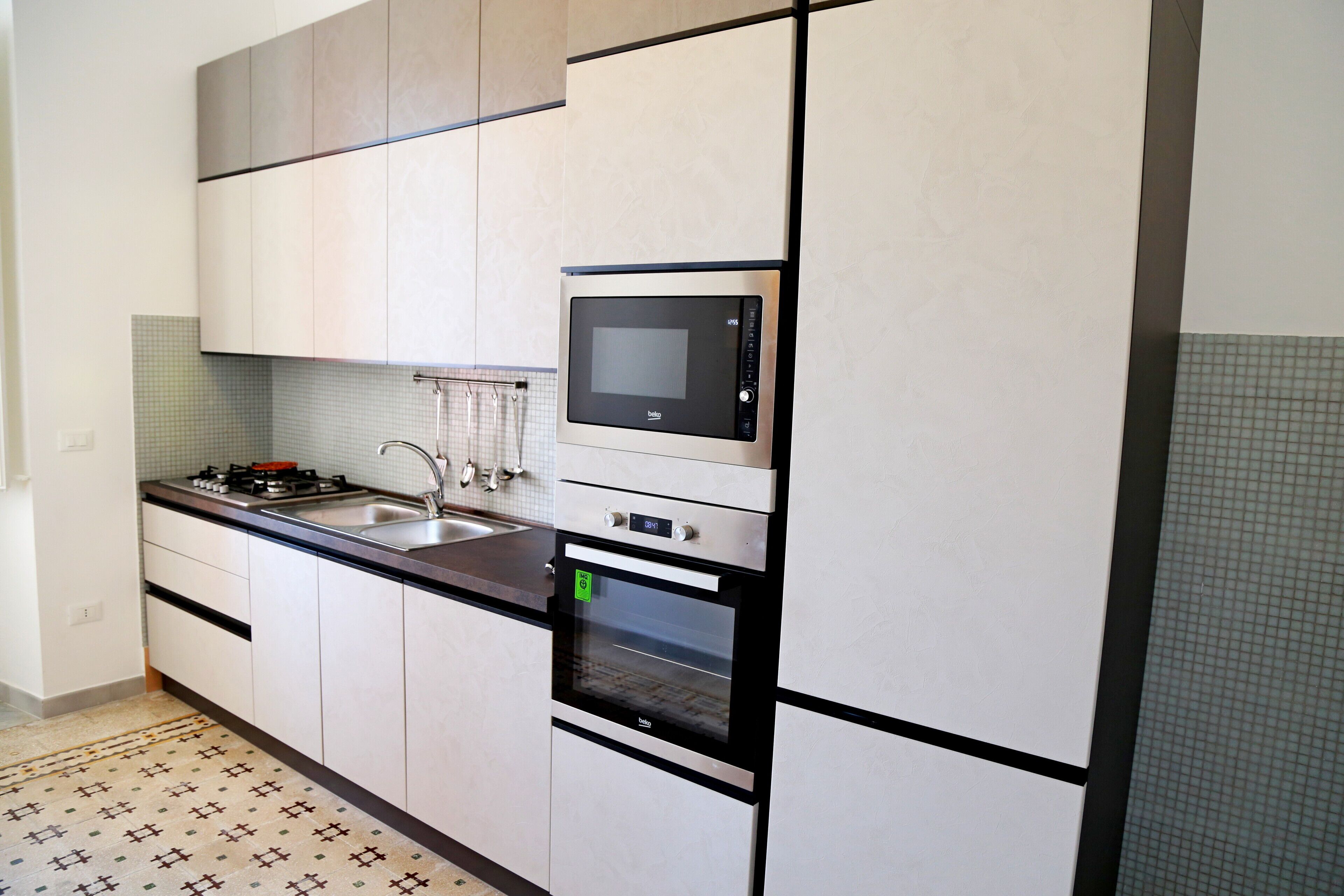 Una cocina moderna con armarios blancos, microondas integrado, estufa y lavamanos.