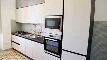 Una cocina moderna con armarios blancos, microondas integrado, estufa y lavamanos.