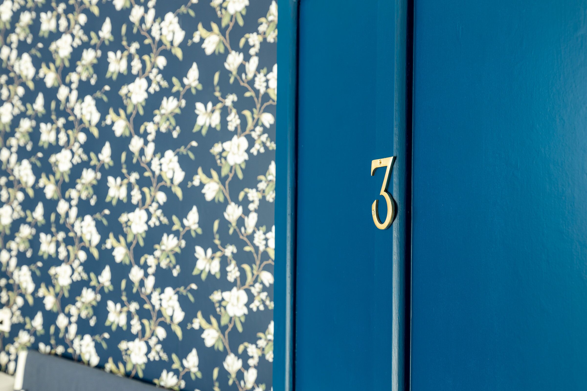Eine blaue Tür mit der Nummer 3, neben einer Wand mit einem floralen Muster.