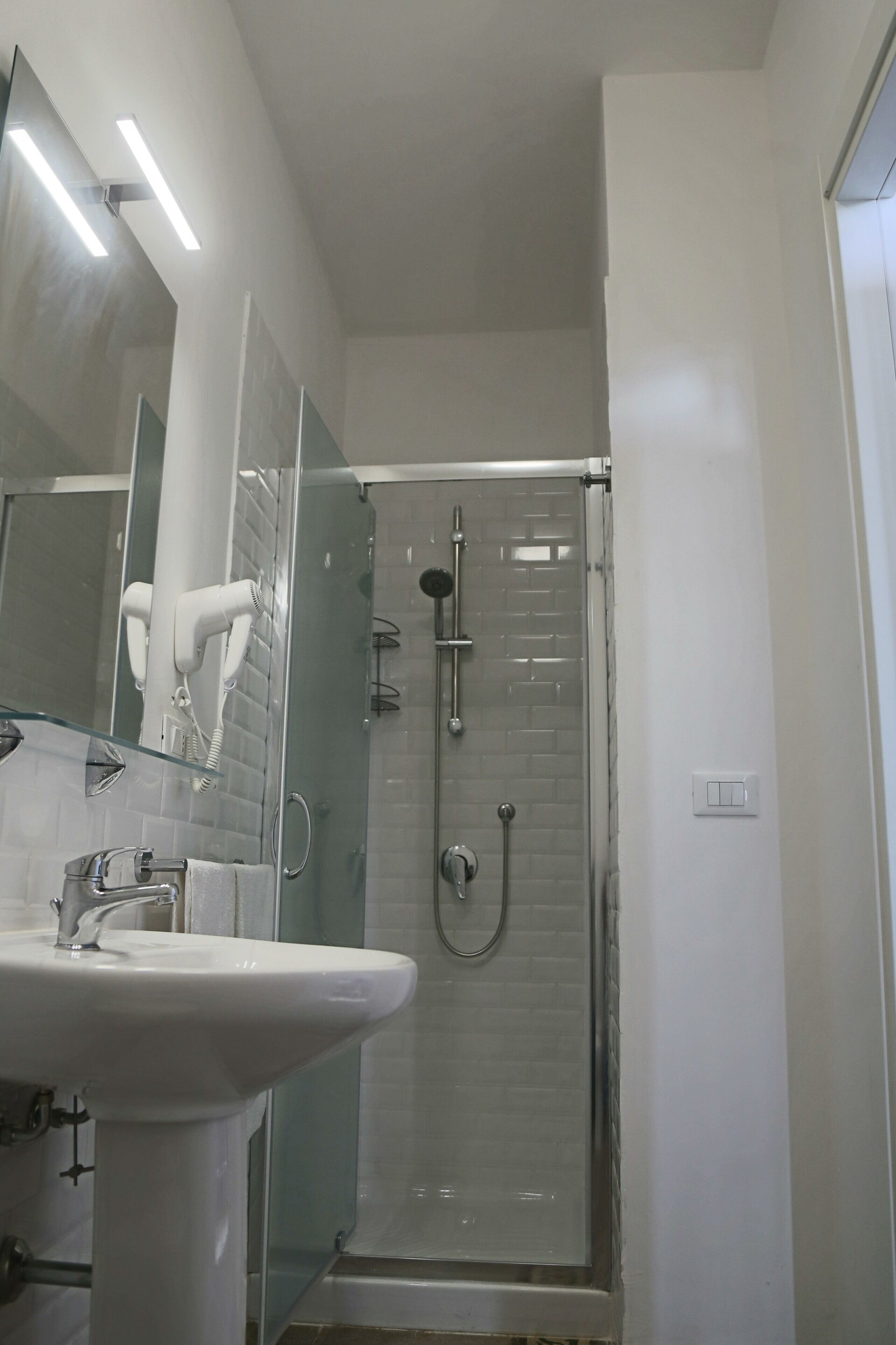 A modern bathroom with a glass-enclosed shower, a white sink, and a hairdryer mounted on the wall.