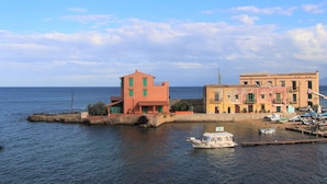 A coastal town with buildings along the waterfront, a small boat docked near the shore, and calm sea in the background. - Villa Edera Rental Rooms (Santa Flavia)