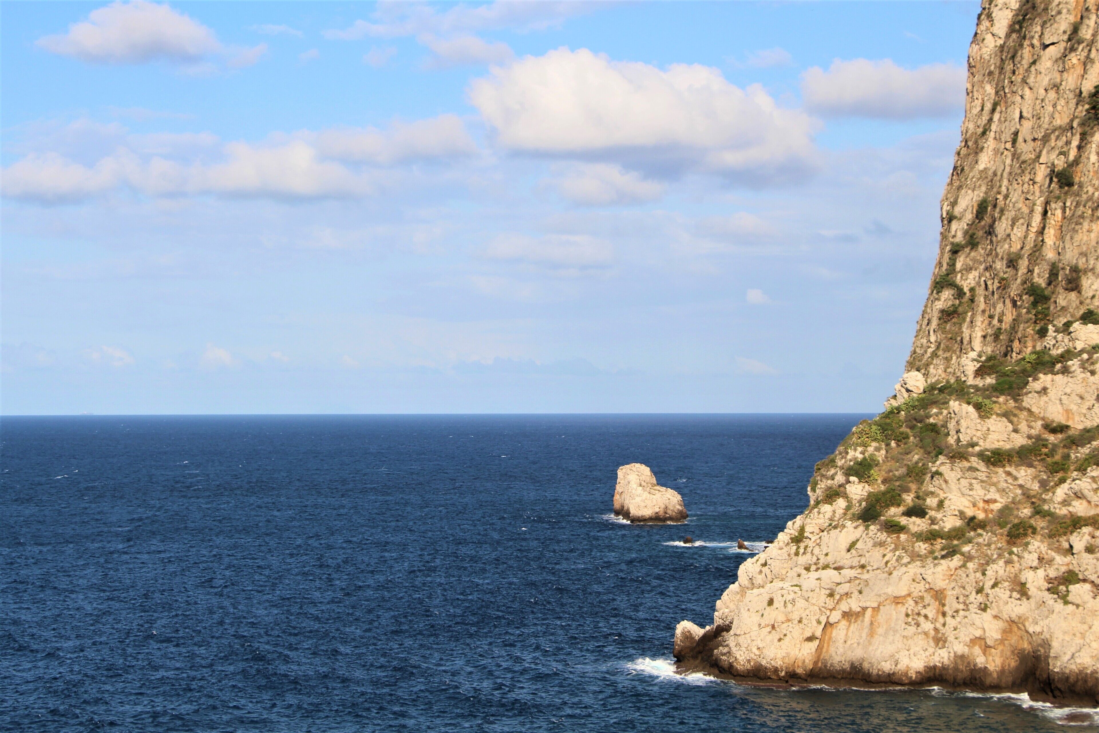 A coastal landscape with a prominent cliff and a small rock formation in the sea.