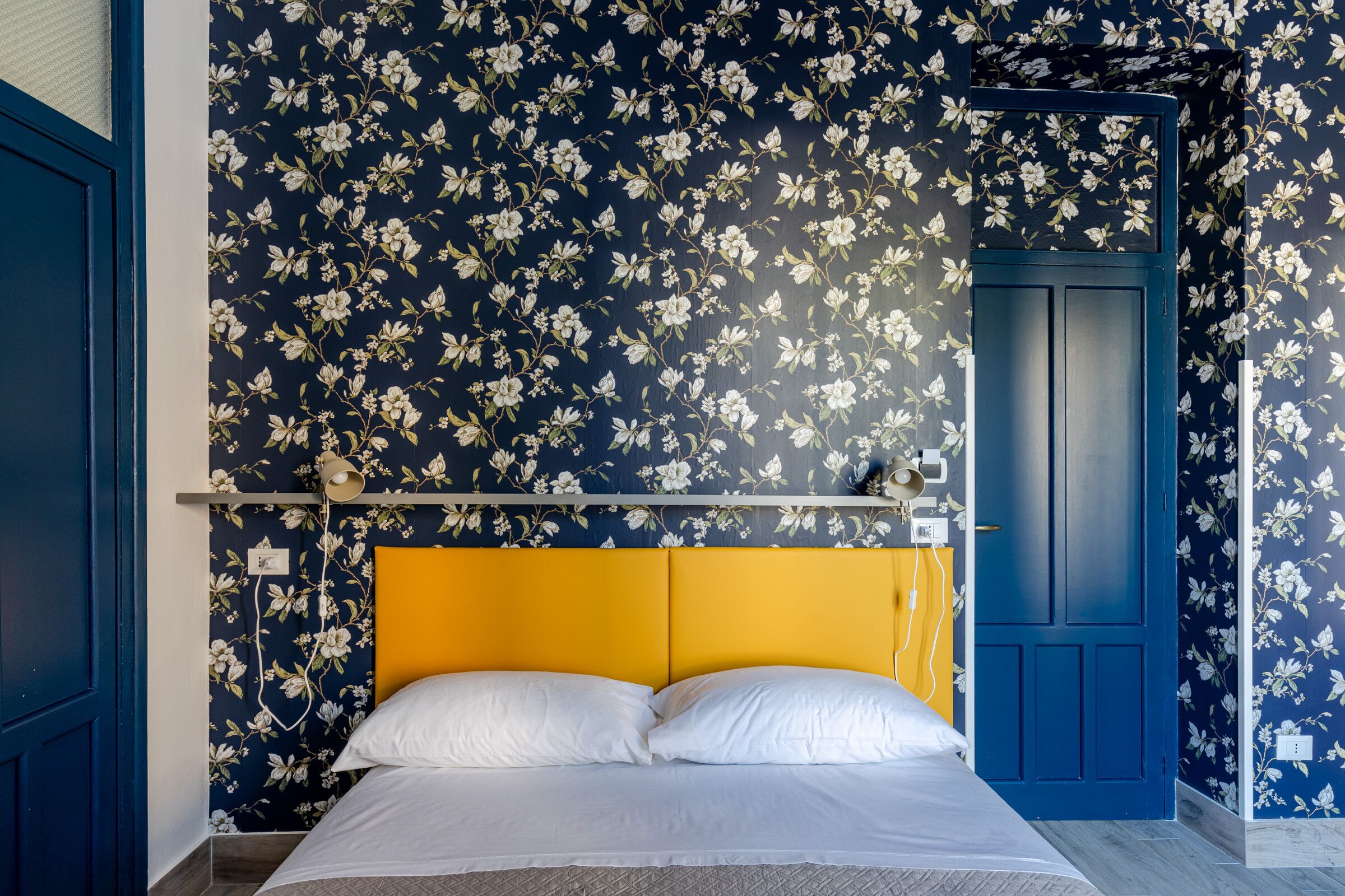 A bedroom with a bed, a yellow headboard, and floral wallpaper.