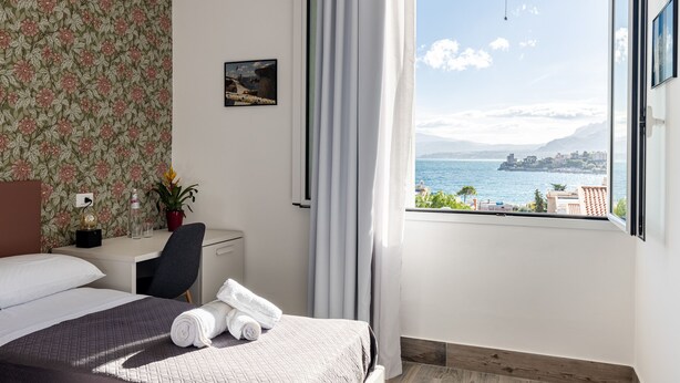 A hotel room with a bed, a desk, a chair, a potted plant, and a view of the sea. - Villa Edera Rental Rooms (Santa Flavia)