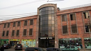 A hotel with a curved glass facade, multiple windows, and a storefront with various shops. - Nice Hotel Yerevan (Yerevan)