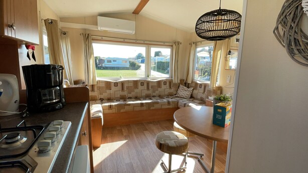 A compact kitchen with a built-in stove, a coffee maker, and a window seat with cushions.