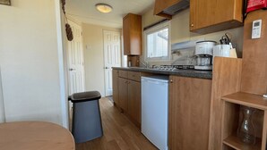A compact kitchen with wooden cabinets, a built-in dishwasher, a coffee maker, and a window providing natural light.