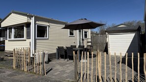 Una casa móvil con un área de patio, que incluye una mesa y sillas, y un cobertizo pequeño.