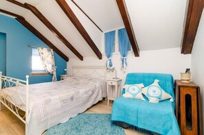 Ein Schlafzimmer mit einem Bett, einem blauen Sessel, einem Nachttisch und einem Fenster mit Vorhängen.