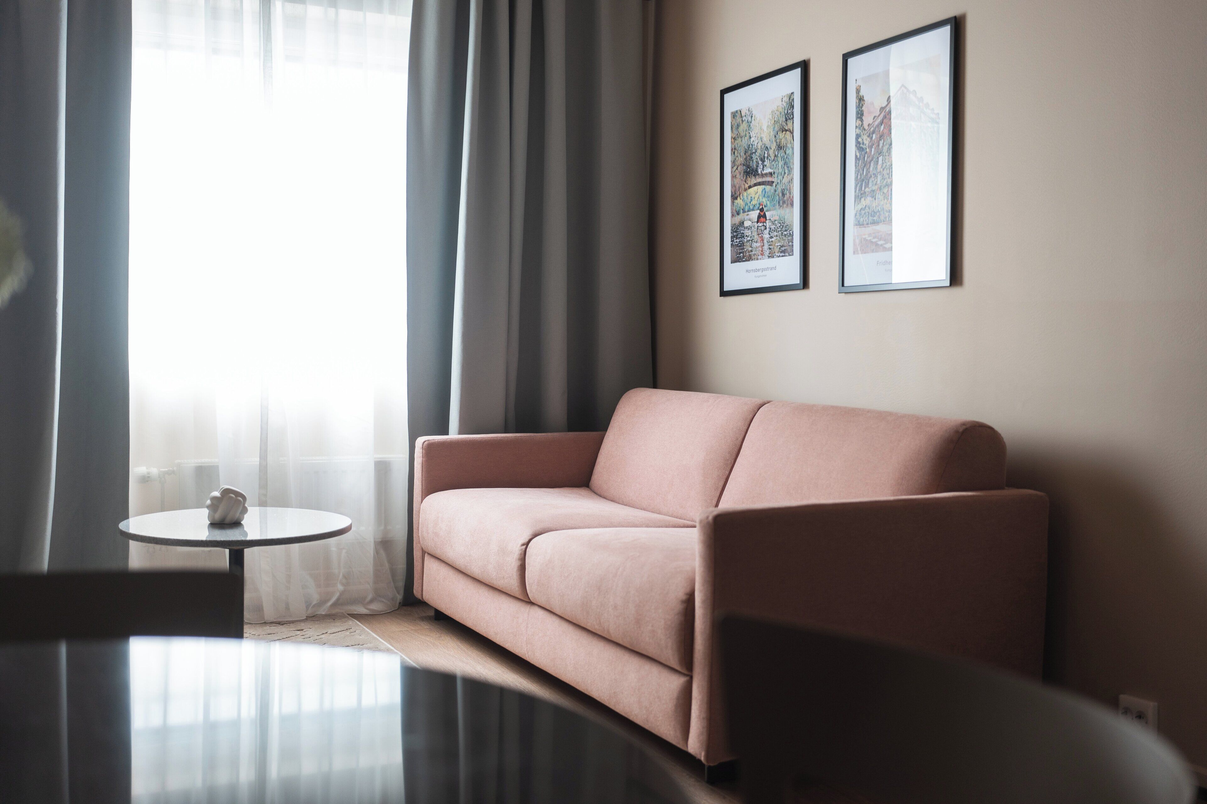 Een moderne woonkamer met een bank, een klein rond tafeltje en twee ingelijste foto’s aan de muur.