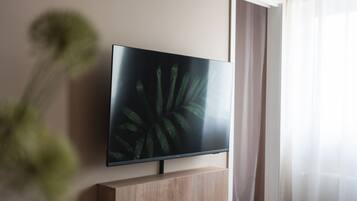 A flat-screen TV mounted on a wooden stand in a room with a plant in the foreground.
