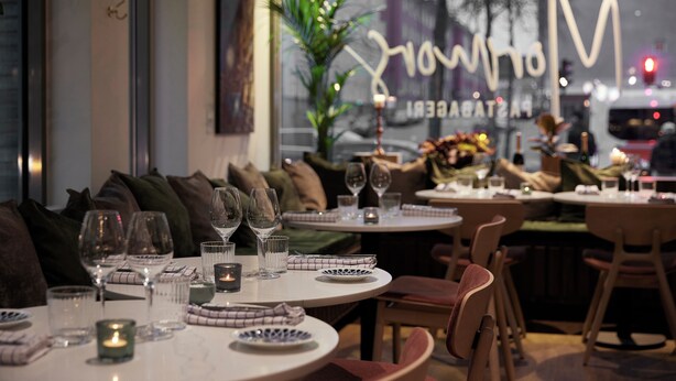 Een restaurant met ronde tafels, gedekt voor een diner, met glazen en kaarsen.