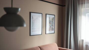 Une pièce comprenant un canapé, deux tableaux encadrés accrochés au mur, un luminaire suspendu et une fenêtre avec des rideaux.
