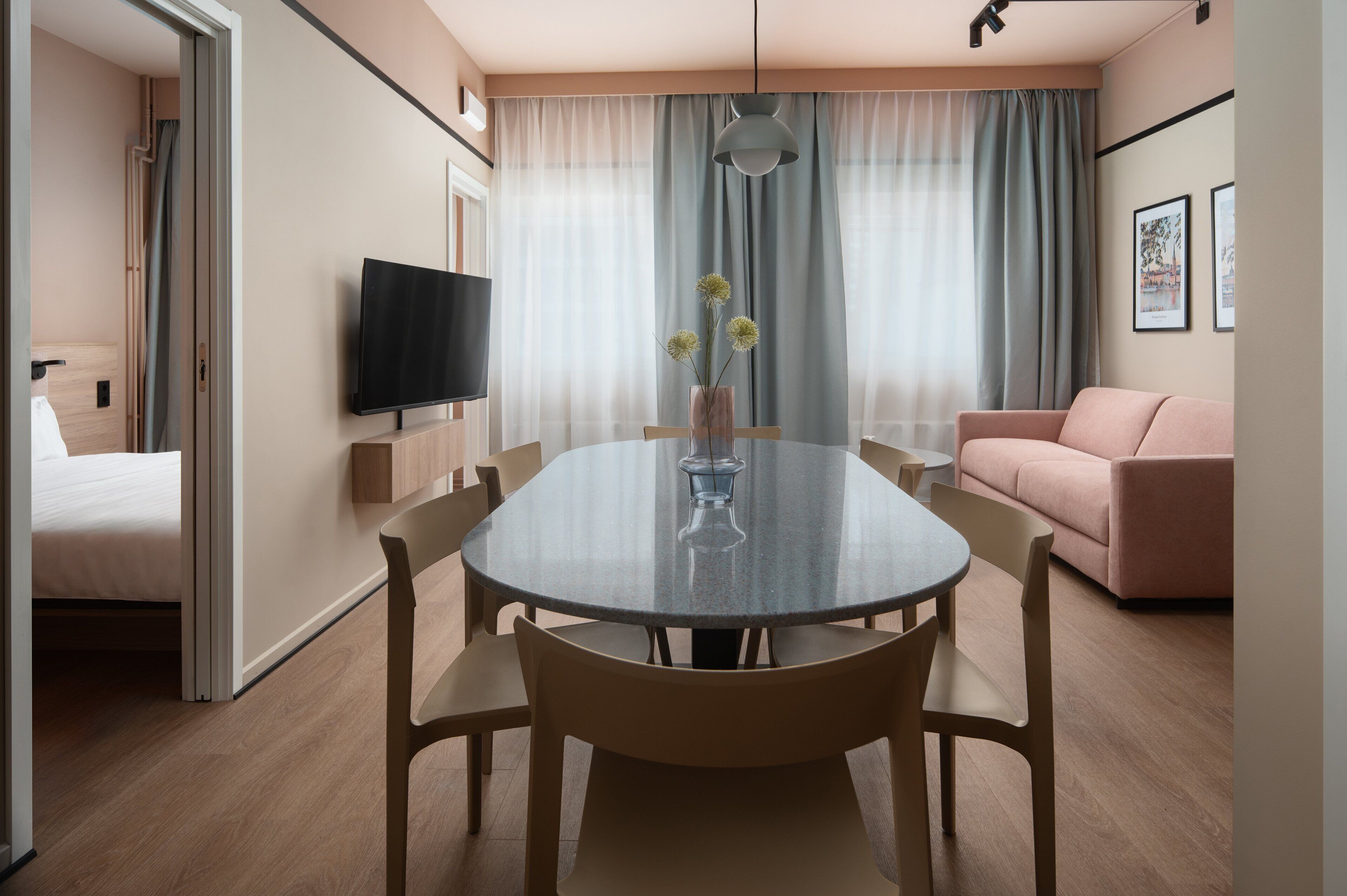A modern hotel room with a round dining table, a sofa, a TV, and a bed.