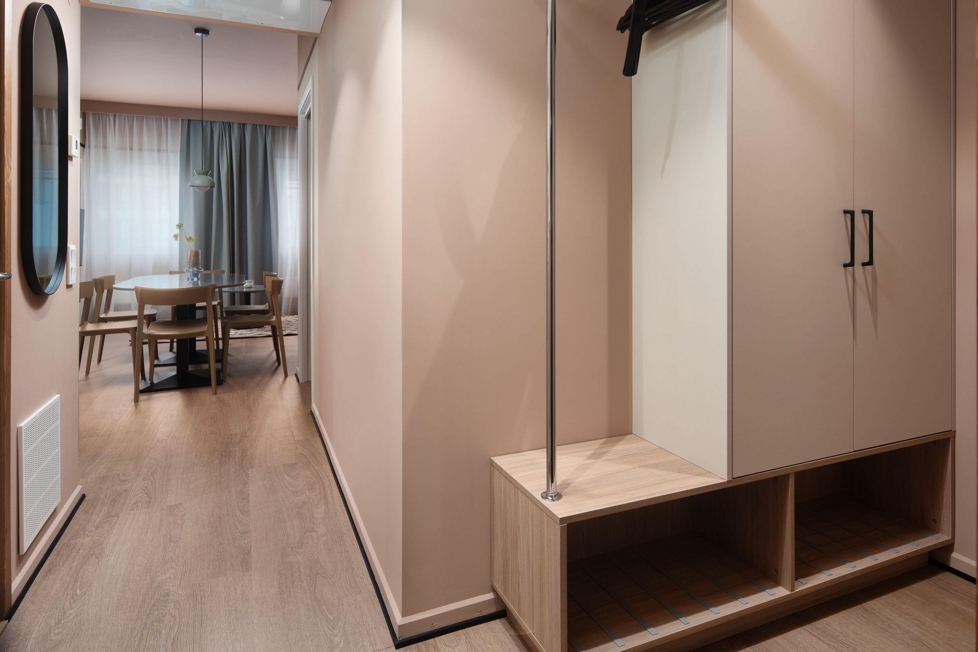 Una habitación moderna con piso de madera, una mesa de comedor con sillas, un espejo grande y un armario con espejo.