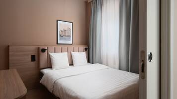A hotel room with a bed, a bedside table, a framed picture on the wall, and a door with a handle.