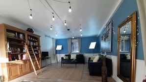 A spacious living room with a wooden bookshelf, a black sofa, a coffee table, and a patterned rug. - Cottage for 10 p max / Private swimming pool / Pond / Ideal location / Paris less 1 hour (La Chapelle-Rablais)