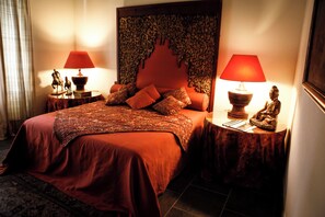 Une chambre d’hôtel avec un grand lit, deux tables de chevet avec des lampes, une tête de lit décorative et une petite statue posée sur l’une des tables.