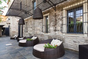 A stone building with outdoor seating, including wicker sofas and chairs, and a pergola with hanging lamps.