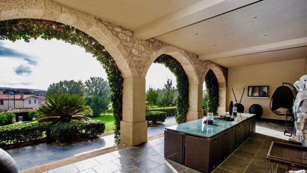 A covered outdoor area with stone arches, a central island table, and a view of the surrounding landscape. - Location Sardinia Borgo Antico XIX (Gesturi)