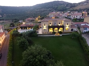 A large stone building with a courtyard, surrounded by smaller houses, set in a hilly area.