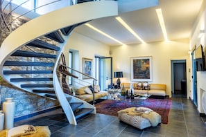 A modern interior with a spiral staircase, a living room with a sofa and coffee table, and a painting on the wall. - Location Sardinia Borgo Antico XIX (Gesturi)