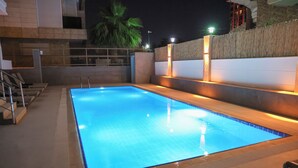 Une piscine rectangulaire dont le bord est recouvert de carreaux, entourée d’un petit muret à surface texturée.