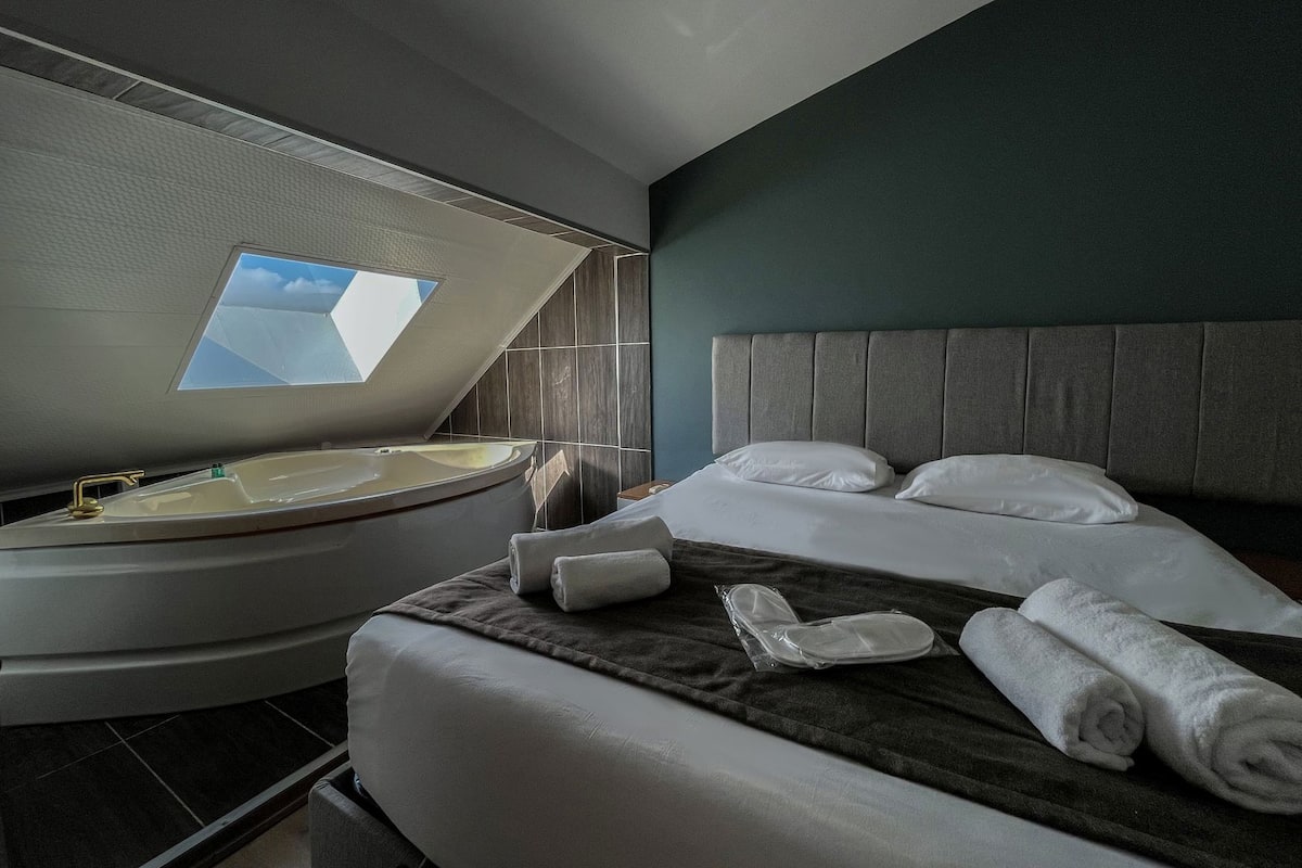 Ein modernes Hotelzimmer mit Dachfenster, einer runden Badewanne, einem großen Bett mit Kissen und einem ordentlich bezogenen Bett.