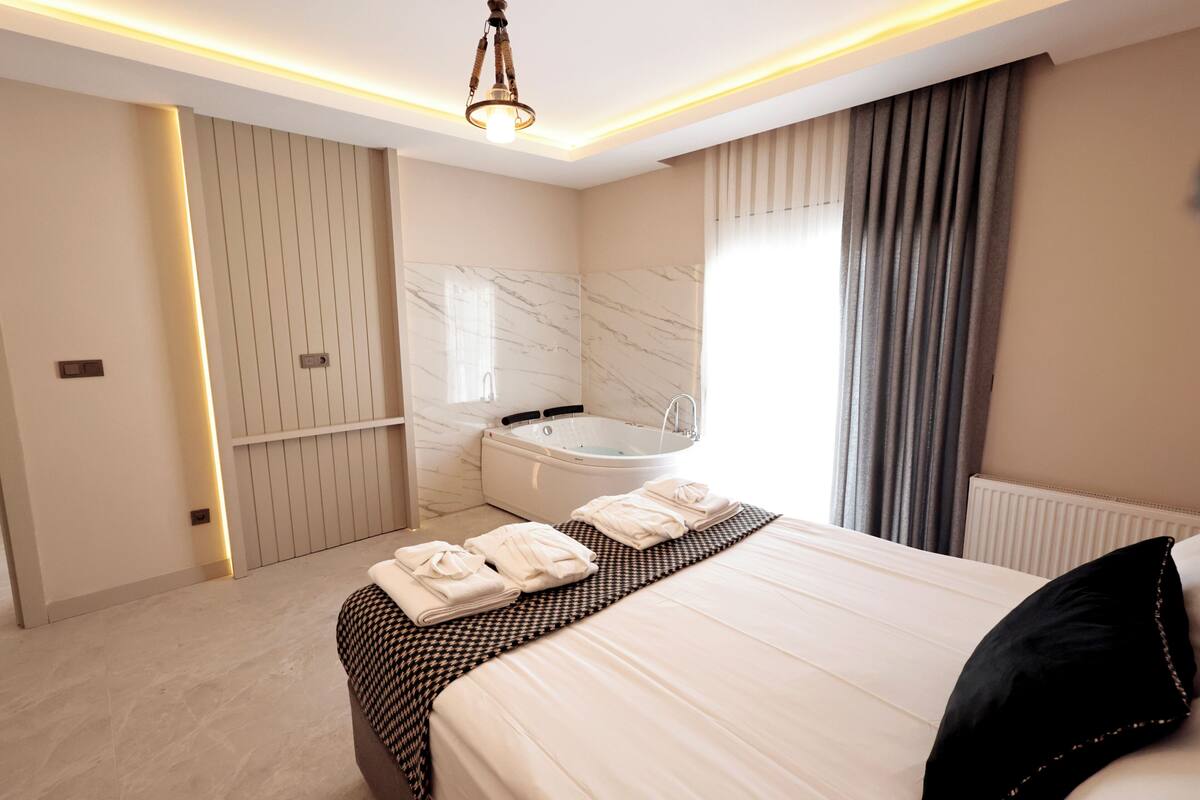 Ein modernes Hotelzimmer mit einem großen Bett, einer integrierten Badewanne und einem großen Fenster mit Vorhängen.