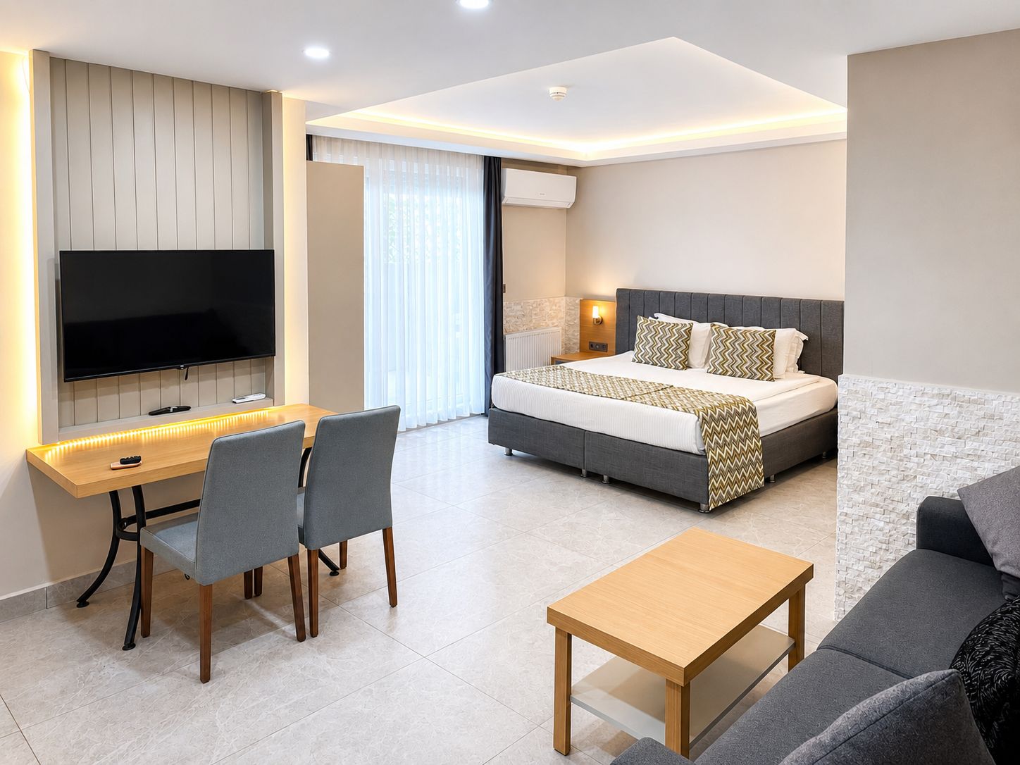 Una habitación de hotel moderna con una televisión de pantalla plana, un escritorio con sillas, una cama con cubrecama estampado y un sofá.