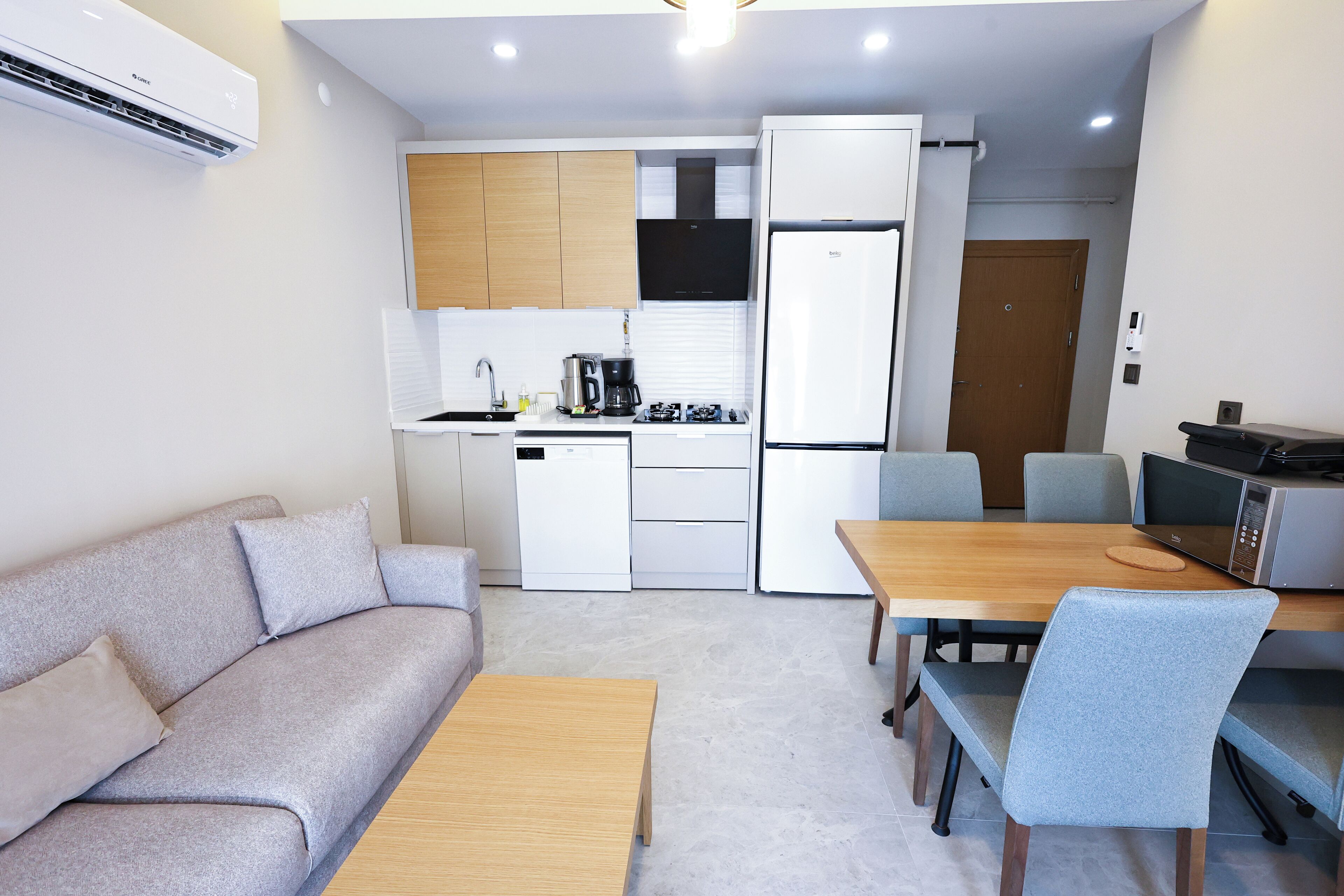 Cocina compacta con cafetera, refrigerador y microondas. Cuenta con un sofá y una mesa de comedor con sillas.