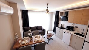 Ett modernt hotellrum med en matplats, en soffa, ett kök med diskho och spishäll samt en luftkonditioneringsanläggning som är monterad i taket.
