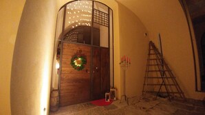 A wooden door with a wreath and a red mat, a candelabra with candles, and a ladder leaning against the wall.
