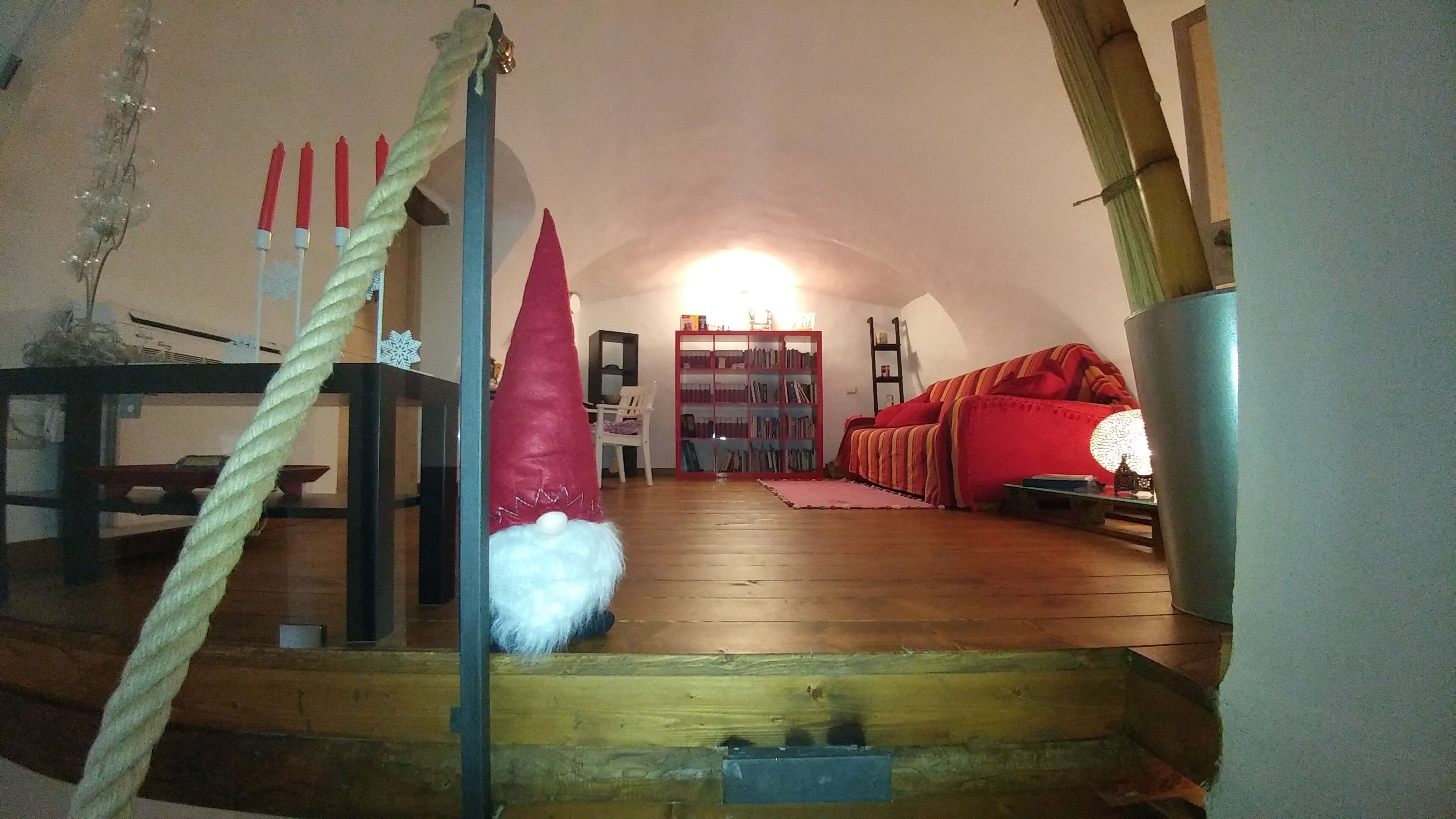Ein gemütliches Dachzimmer mit Holzboden, einem roten Sofa, einem Bücherregal und einer dekorativen Gartenzwerg-Figur.