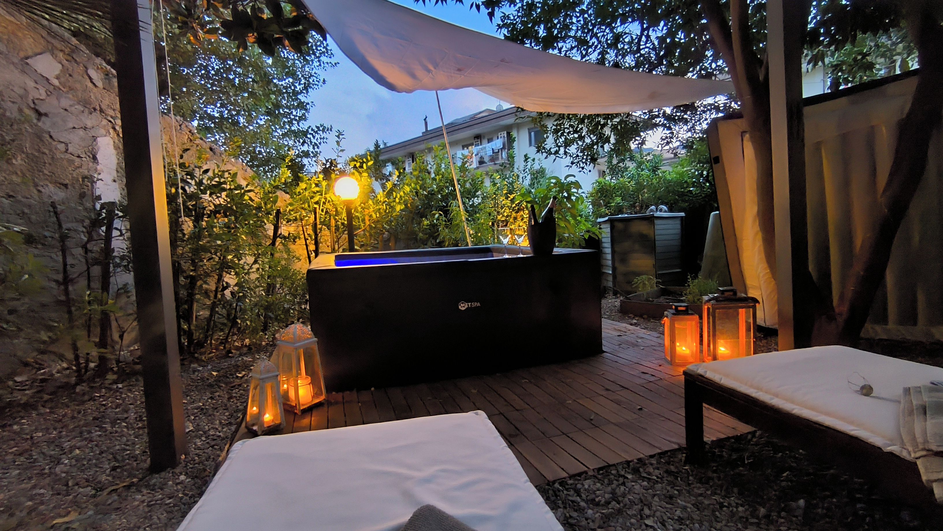 Ein Whirlpoolbereich mit Holzterrasse, umgeben von Grün und einem Gebäude im Hintergrund.