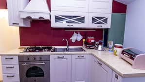 Una cocina con armarios blancos, un horno de acero inoxidable, una estufa a gas, un fregadero y diversos utensilios de cocina sobre la encimera.