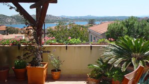 Eine Terrasse mit Blumentöpfen, Meerblick und Hügeln in der Ferne.