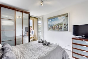 A hotel room with a bed, a television, a painting, and a sliding door to a balcony.