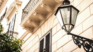 A street lamp attached to a building with ornate architectural details and a window with shutters. - Residence Torremuzza - Charming House In The Heart Of Palermo With Lovely View (Palermo)