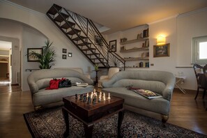A living room with two sofas, a coffee table, a chessboard, a staircase, and bookshelves.