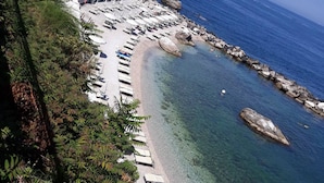 Une plage côtière aux eaux cristallines, bordée d’un rivage rocheux, et un bâtiment doté d’une terrasse offrant une vue sur la mer.