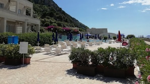 Un espace piscine agrémenté de chaises longues et de parasols, entouré de plantes en pot et avec une chaîne de montagnes en toile de fond.