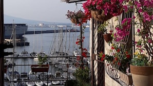 Un balcon agrémenté de plantes et de fleurs en pot, donnant sur une marina où sont amarrés des bateaux.