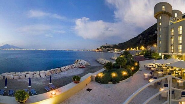 Un hôtel situé sur la côte, offrant une vue sur la mer, avec une plage de rochers et des espaces de détente en plein air.